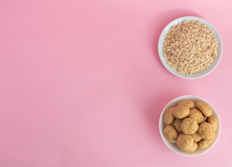 Flatlay oatmeal, oatmeal cookies on a white plate on a pink background, top view, healthy eating concept, and making cereal or cookies. A place for text on the left. High-quality photo