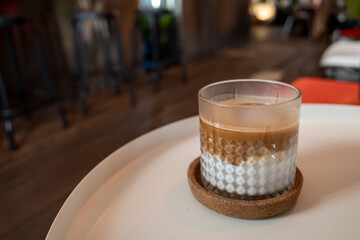 Transparent Glass Cup of latte, flat white or piccolo coffee on white coffee table and blur interior cafe.
