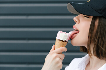Brunette girl in a cap and shirt eats fun ice cream - obrazy, fototapety, plakaty