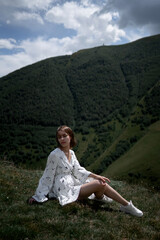 Brunette girl in white on the background of the green mountains.