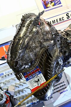 Steel scary head of Tyrannosaurus Rex made of engine parts and other industrial components welded together with catalogue of Commerc Service distributor in his jaws, displayed as advertisement on expo