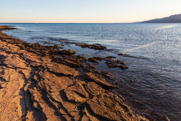 Stony ground of the coast in Lagoon beach, the Red Sea and mountains on the horizon. Dahab, South Sinai Governorate, Egypt