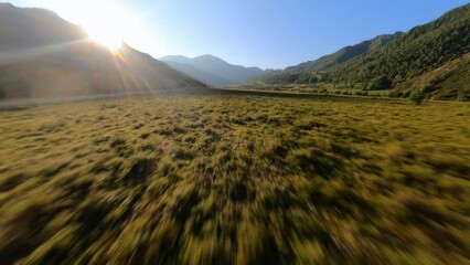 Speed aerial view flying over autumn spring grass plant natural mountain valley organic environment sunlight. FPV sport drone fast low flight picturesque river flow water stream and dirt road path way