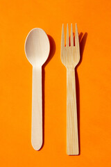 Wooden eco bamboo cutlery spoon and fork on bright orange background. Meal time concept
