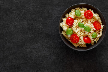 Fusilli pasta cooked with tomatoes and basil on dark background, top view, space to copy text.