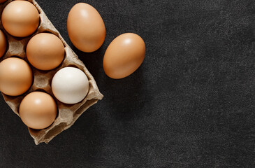 Chicken eggs, in a cardboard tray, on dark background, top view, space to copy text.