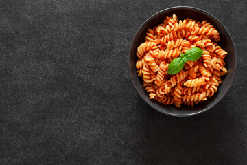 Fusilli pasta cooked with tomatoes sauce and basil on dark background, top view, space to copy text.