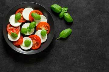 Caprese, antipasto appetizer, on a grey plate, and basil leaves on dark background, top view, space...