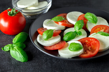 Caprese, Iitalian appetizer of mozzarella, tomatoes and basil, on dark background, selective focus.