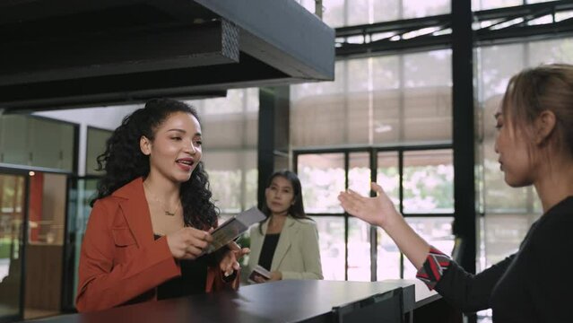 Happy Asian woman tourist check in at counter lobby hotel for resting while travel on vacation summer. Young female model giving her passport to officer at check-in counter in international airport. 