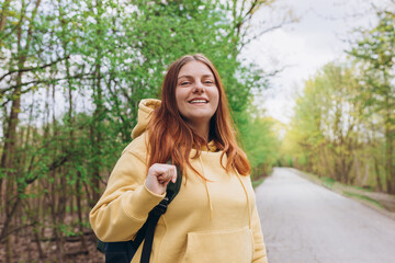 Young cheerful redhaired woman enjoying spring day in park. Young woman hiking and going camping in nature. Person with backpack walking in the forest