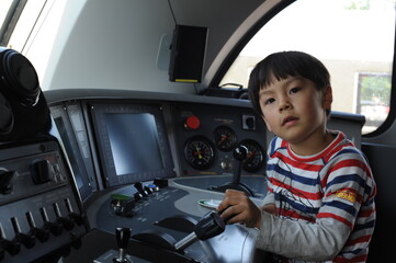 A young boy steering a locomotive and train in a driving compartment or cabin with handles and meters as a train driver, engine driver, engineman, locomotive driver, engineer, locomotive handler