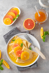 Delicious crepes suzette with orange syrup and slices fruits on a plate on a gray concrete background, top view