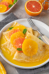 Delicious crepes suzette with orange syrup and slices fruits on a plate on a gray concrete background, top view