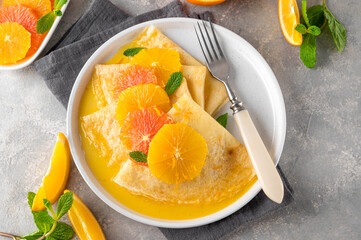 Delicious crepes suzette with orange syrup and slices fruits on a plate on a gray concrete background, top view