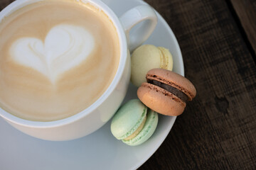 Cup of cappuccino served with colorful small macaroons. Close up