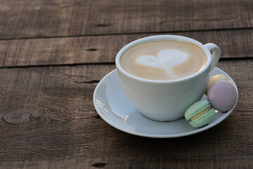 Cup of cappuccino with colorful small macaroons on a wooden table