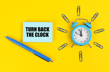 On the yellow surface there is an alarm clock, a pen and stickers with the inscription - Turn Back the Clock - Powered by Adobe