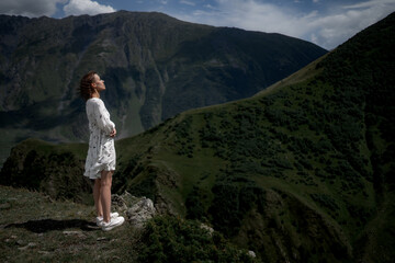 Naklejka premium Slim brunette girl in a white dress is walking in the mountains.
