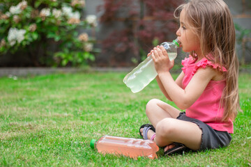 Drink with electrolytes in a transparent bottle in the hands of a happy child on a green lawn in a pink T-shirt