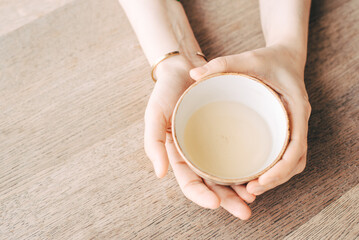Women's hands hold a cup of tea at a table in a cafe.