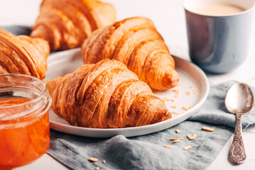 Plate with fresh croissants, jam and coffee on white wooden table. Close up.