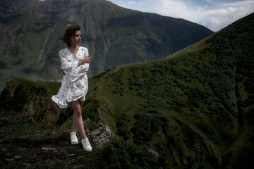 Sensual cute girl with brown short hair in a white dress is looking away against the backdrop of mountains.