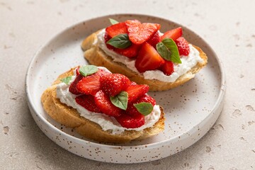 Bruschetta with ricotta, strawberries and basil on light background. Comfort food. Copy space. Selective focus.