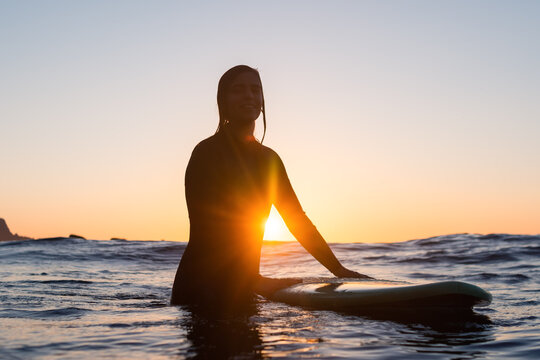 Surfer Girl Waiting For A Wave In The Water At Sunset