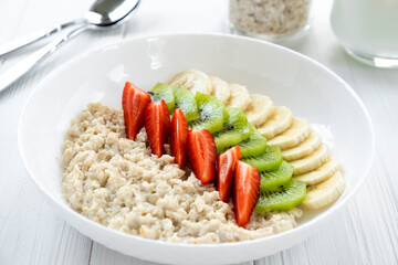 Homemade oatmeal porridge with fresh fruits, strawberry, banana, kiwi. Recipe of healthy breakfast full of vitamins and antioxidants, clean eating.