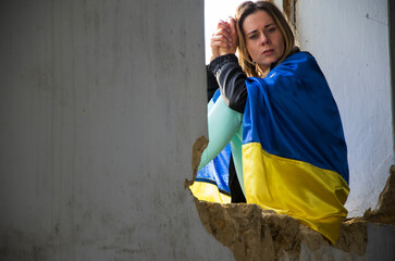 War in Ukraine. The woman is wrapped in the Ukrainian flag. Ukrainian woman in ruins. Consequences...