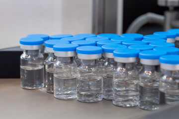 Many medical injection glass vials with blue tops and liquid - close up, selective focus. Pharmaceutical industry, medicine and laboratory equipment concept