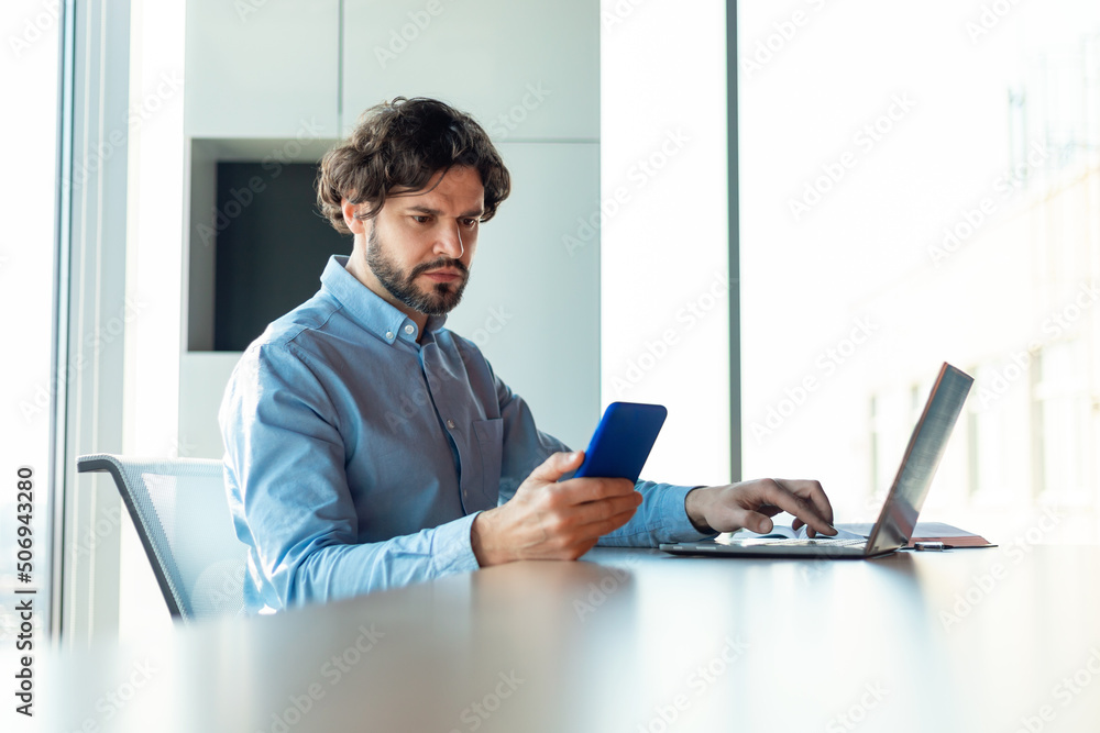 Poster portrait of focusedman using smartphone and pc at office
