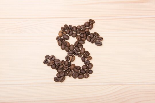 Wooden craft surface as a comfortable background wall or floor with different structures of light wood full of many coffee beans . A dollar sign shaped coffee beans. In the middle of the surface.