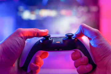 Close-up of a modern gadget - gamepad. A gamer plays video games online with friends on a big TV screen. Game strategy, virtual reality, cyberspace, electronics, dartless technologies. © Anton