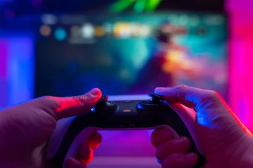 Tuinposter Close-up. Modern gamepad. A gamer plays video games on a technological background on a TV screen. Virtual reality, entertainment, communications, cyberspace. © Anton