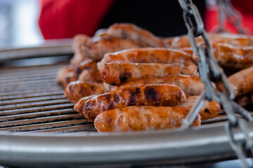 Process of grilling fresh meat sausages on big round hanging grill at summer local food market: close up view. Outdoor cooking, barbecue, gastronomy, cookery, street food concept