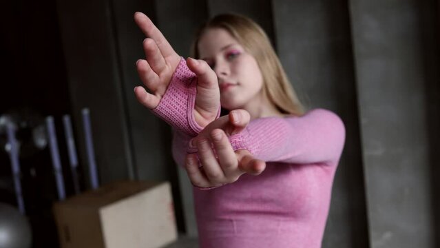 Young girl teenager doing stretching in gym. Blond woman gymnast ballerina dancing at wooden bench. Girl in pink sports suit doing acrobatic figures and string. Long-haired 16-year- old girl do sports