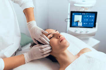 Cosmetologist making ultrasonic cleaning and rejuvenation the face to beautiful woman on the spa...