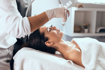 Obraz na płótnie Canvas Cosmetologist making ultrasonic cleaning and rejuvenation the face to beautiful woman on the spa center.