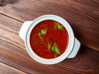 Close-up of soup borscht in a white ceramic soup bowl on a wooden background. Traditional soup for Russia and Ukraine. Greens float on top of the soup. Top view, flat lay