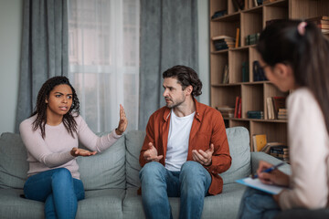 Angry young black wife ignoring european husband on consultation with psychiatrist in clinic interior