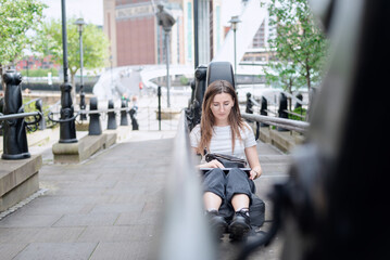 Fototapeta premium A sad girl opens her laptop sitting on the parapet in the park.