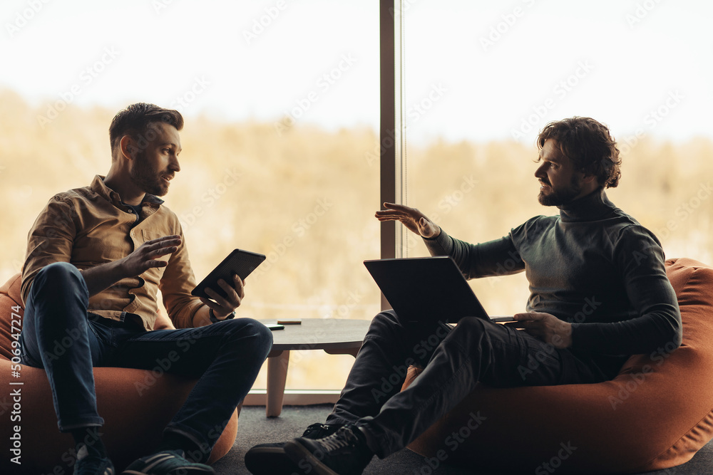 Poster male colleagues using portable computers and discussing business project, working together, discussi