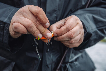 Fisherman changing spinner tail lure on spinning. Fishing on an overcast spring day.