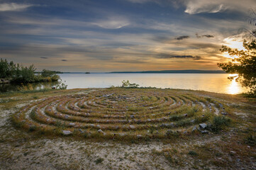Stone labyrinth on the background of the sunset river