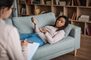 Obraz premium Serious young african american female patient lies on couch, consultation with european lady doctor