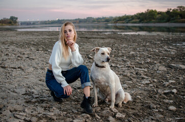 Portrait a beautiful young woman in a white sweater with her white dog outdoors full-length.
