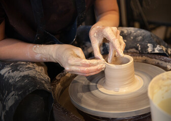 A woman works on a potter's wheel. Hands form a cup of wet clay on a potter's wheel. Artistic...