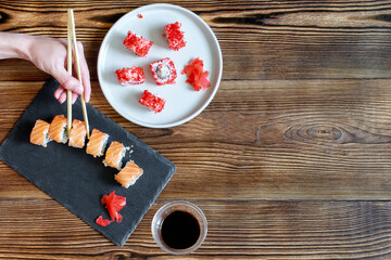 Woman hands holding fish sushi rolls with salmon, red caviar with chopsticks on gray black ceramic...
